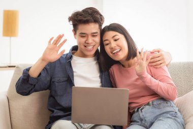 Çinli bir çift evdeki koltukta oturan dizüstü bilgisayarla çevrimiçi video çekiyor. Eşler Aile Üyelerini Arıyor Ekrana Merhaba El sallıyor. Uzak İletişim Konsepti