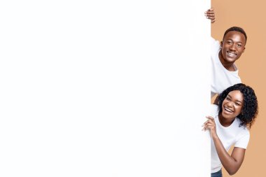 Reklam için boş pankartın yanında duran gülümseyen siyah adam ve kadın. Neşeli Afro-Amerikan çift reklam için boş pano tutuyorlar ya da sarı stüdyo arka planı, panorama