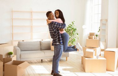 Mutlu taşınma günleri. Sevgi dolu siyah adam yeni evlerinde güzel kız arkadaşını kucaklıyor ve kaldırıyor, panorama. Genç Afrikalı Amerikalı aile yeni bir daireye taşınacağı için heyecanlı.