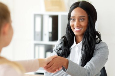 Tanımlanamayan siyahi İK yöneticisi, iş görüşmesinde kadın işverenle el sıkışıyor. Yeni çalışanla anlaşma yapan kafa avcılığı uzmanının portresi.