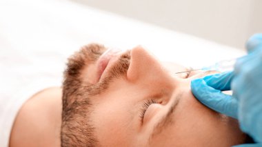 Orta yaşlı bir adamın estetik kliniğinde burnuna güzellik iğnesi vurulması. Estetik cerrah yakışıklı sakallı adama yaşlanma önleyici iğne yapıyor. Erkek kozmetolojisi, estetik tıp konsepti