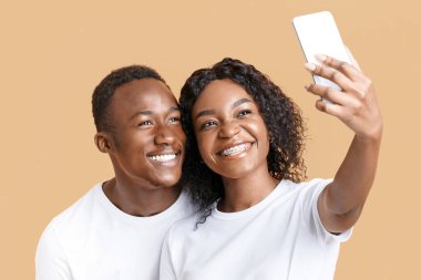 Mutlu Afro-Amerikan çifti akıllı telefondan selfie çekiyor. Stüdyo üzerinden, fotokopi alanı üzerinden. Neşeli genç siyah erkek ve kadın aşıklar bağlanırken, cep telefonu kullanarak fotoğraf çekiyorlar.