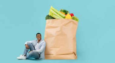 Müşteri, çeşitli taze sebzeler ve meyvelerle dolu büyük bir kesekağıdının yanında gevşer. Bu ayar, modern market alışverişini yansıtıyor..