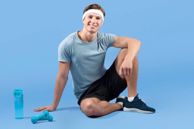 Dambılları ve bir şişe suyu olan genç bir atletin uzun portresi eflatun stüdyo arka planında oturuyor. Milenyum sporcusu kameraya bakıyor ve gülümsüyor, antrenmandan sonra dinleniyor.