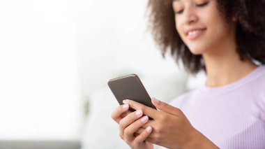 Covid-19 kilitlenirken modern online iletişim, evde yalnız, yeni normal, güvende ol. Neşeli, Afro-Amerikan bir kadının mesaj yazması ya da oturma odasında telefonla sörf yapması, seçici bir odak noktası.