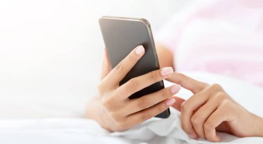 İnternette sörf yapmak, covid-19 karantinası sırasında modern cihazlarla blog yazıları yazmak. Afro-Amerikalı genç bayan yatakta uzanıyor ve yatak odasının içinde akıllı telefonuyla yazı yazıyor. Kapalı, boş alan, kırpılmış.