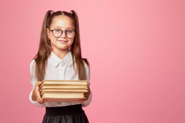 İnek ve zeki çocuk. Gözlüklü ve üniformalı şirin küçük kız pembe arka planda izole edilmiş kitaplar tutuyor.