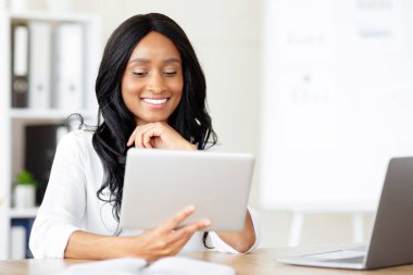 İş yerinde tablet kullanan neşeli siyahi iş kadını web kamerasından iş arkadaşlarıyla konuşuyor. Başarılı milenyum CEO 'su önemli belgeyi çevrimiçi okuyup e- postaları kontrol ediyor