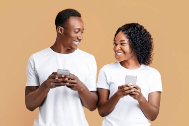 Gülümseyen Afro-Amerikan erkek ve kadın birlikte oynuyorlar ve akıllı telefonlarda video oyunlarında yarışıyorlar, sarı stüdyo geçmişi. Neşeli siyah çift çevrimiçi oyunlar oynuyor.