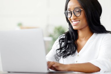 Ofisteki klavyede dizüstü bilgisayar ve daktilo kullanan mutlu bir kadın şirket çalışanı. Genç siyahi sekreter e-posta yazıyor, iş bilgilerini internette arıyor, online konferans yapıyor.