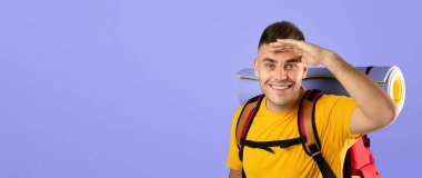 Kamp malzemeleri ve haritasıyla mavi stüdyo arkaplanındaki kameraya bakan mutlu bin yıllık turistler. Gülümseyen yakışıklı sırt çantalı seyahat rotasını çiziyor.