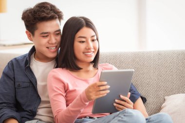 Çinli erkek arkadaş ve dijital tabletli kız arkadaş çevrimiçi film izliyorlar evdeki oturma odasında kanepede oturup rahatlıyorlar. Modern Gadget 'lar, Asyalı Aile Yaşam Tarzı Konsepti