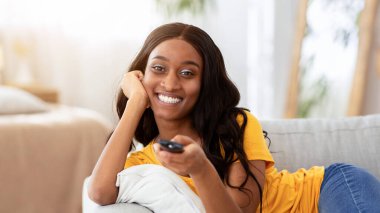 Hafta sonu eğlence aktiviteleri. Milenyum siyahi kadın uzaktan kumandalı TV kanallarını değiştiriyor, uzayı kopyalıyor. Mutlu Afro-Amerikalı kadın TV 'de ilginç bir program izliyor.