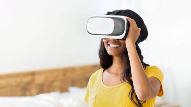 Etkileşimli eğlence konsepti. Sanal gerçeklik kulaklığı takmış genç siyahi bir kadın siber uzayı keşfediyor ya da evde oyun oynuyor. Kilitlenme hobileri ve gelecek teknolojileri