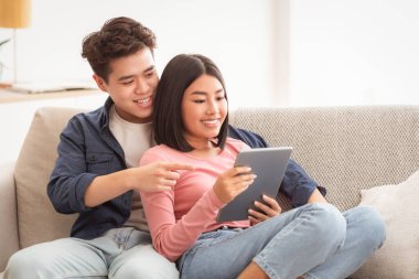 Mutlu Asyalı eşler evdeki oturma odasındaki koltukta oturan dijital tablet üzerinde interneti tarıyor. Koreli kız arkadaş ve erkek arkadaş birlikte bilgisayar kullanıyor. Modern Gadgets Yaşam Biçimi Konsepti