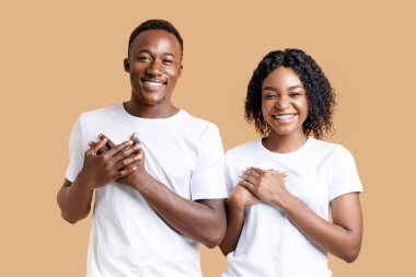 Minnettar Afro-Amerikalı çift her iki avuçlarını göğsünde tutuyor ve gülümsüyor, minnettarlıklarını ve iyi hislerini dile getiriyorlar, sarı stüdyo geçmişi. Mutlu siyah adam ve kadın daha iyisini umuyor.