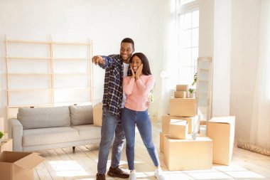 Mutlu siyah adam heyecanlı kız arkadaşına sarılıyor, mobilya yerleştirme hayalleri kuruyor, yeni evi işaret ediyor. Milenyum çifti yeni bir daireye taşınıyor. Yer değiştirme günü konsepti