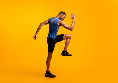 Yüksek dizler. Enerjik afro adam spor yapıyor, bacağını kaldırıyor ve kolunu sallıyor.