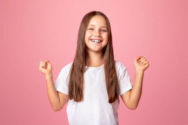 Mutluluk ve zafer duyguları. Küçük çocuk zevk veriyor ve yumruklarını kaldırıyor, pembe arka planda izole edilmiş, boşluğu kopyalıyor.