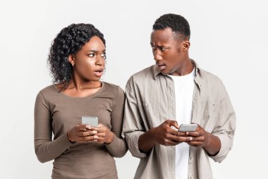 İlişkilere güvensizlik. Akıllı telefonları olan ve gri stüdyo arka planından birbirlerine bakan kızgın siyah bir çift. Afrika kökenli Amerikalı erkek ve kadın evliliklerinde zorluklar yaşıyor.