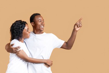 Neşeli siyah adam sarı stüdyo arka planında kız arkadaşına fotokopi odasını gösteriyor. Afro-amerikan aşıklar, reklam, metin ve panorama için boş alana bakıp sarılıyorlar.