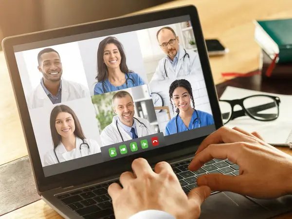 Ofisteki Dizüstü bilgisayar kullanan çeşitli meslektaşları arayan Erkek Doktor 'un yakın çekimi. Video konferansı sırasında çok ırklı kadın ve erkek tıbbi işçilerle bilgisayara odaklan.