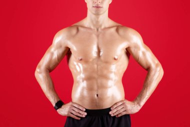 Kırmızı stüdyo arka planında çıplak vücut pozu veren yakışıklı kaslı genç adam. Göğüs kafesi olmayan ve kameraya bakan belirgin kasları olan ciddi bir bin yıllık vücut geliştirici. Spor ve spor konsepti