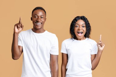 Inspired black man and woman pointing fingers up over yellow studio background. Happy young african american couple having great idea, found solution for their problem, expressing happiness