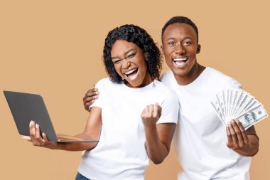 Mutlu Afro-Amerikan milenyumu kutlayan erkek ve kadın dizüstü bilgisayarla ve bir sürü parayla sarı stüdyo arka planında bağırarak ve yumruklarını sıkarak kazandı. Piyango, kumar, online oyun