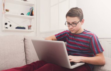 Evdeki kanepede bilgisayarı olan bir genç. Çocuk internete takılmış, klavyede daktilo kullanıyor.