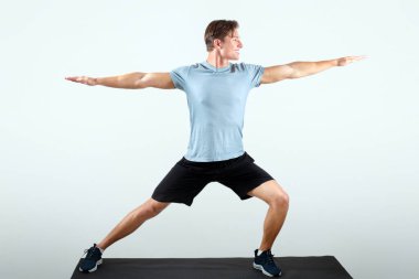 Spor kıyafetli yakışıklı genç adam spor minderinde yoga pozu veriyor. Stüdyonun arka planında, uzun bir portrede. Asana ya da pilates yapan çekici milenyum çocuğu.