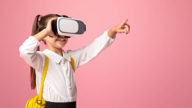 Sanal gerçeklik gözlüklü bir öğrenci pembe arka plandaki stüdyoda pembe arka planı işaret ediyor.
