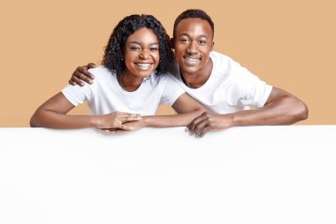 Mutlu Afro-Amerikan çifti sarı stüdyo arka planında boş dikey reklam panosuna yaslanıyor. Neşeli genç siyah erkek ve kadın reklam ya da metin için boş alan gösteriyor.