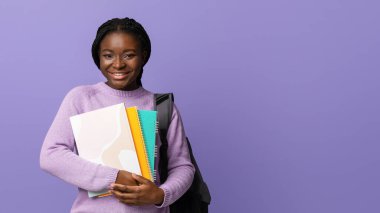 Çalışmaya geri dön. Morarmış arka planda poz veren, üniversite eğitiminden zevk alan, kameraya bakan, fotokopi çeken, çalışma kitapları ve sırt çantasıyla genç, siyah bir üniversite öğrencisi.