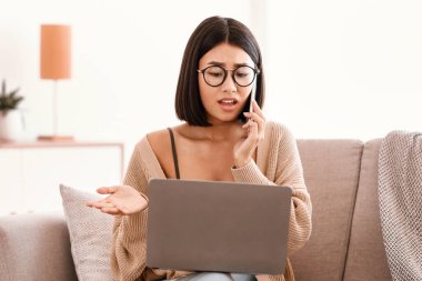 Problem kavramı. Gözlüklü ciddi bir kadın cep telefonuyla konuşuyor, koltukta oturuyor ve dizüstü bilgisayar kullanıyor, internet bağlantısı sorunu yaşıyor, müşteri yardım hattını arıyor.