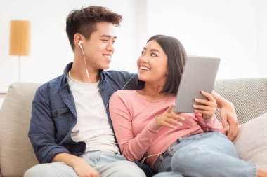 Çinli bir çift tablet bilgisayar kullanıyor. İnternette film seyrediyor. Evde koltukta oturuyor, hafta sonları dinleniyor. Asyalı Kız Arkadaş ve Erkek Arkadaş Hafta Sonu Keyifli Gadget Uygulaması Kullanıyor, İnternet Taranıyor.