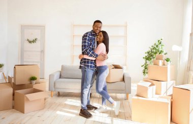 Yeni evlerinin taşındığı panorama gününde karton kutuların arasında kucaklaşan yeni evli romantik çift. Güzel genç kadın ve sevgi dolu kocası oturma odasında kucaklaşıyorlar.