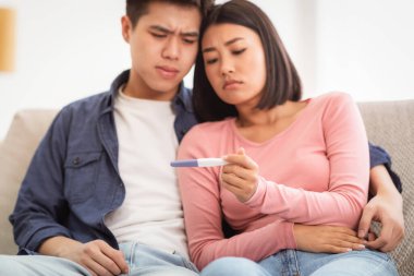 Aile Doğurganlıkla Mücadele. Hüsrana uğramış Japon Çiftin Negatif Hamilelik Testi Evdeki Koltukta Oturuyor. Ebeveyn olmayı hayal eden eşler. Çocuk Doğum Problemi Konsepti. Sığ Derinlik