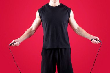 Aerobik konsepti. Kırmızı stüdyo arka planında ip atlayan ciddi bir atletik adam. Kararlı genç sporcu antrenmandan önce kardiyo egzersizleri yapıyor.