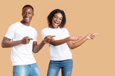 Duygusal Afrikalı-Amerikalı çift gülümsüyor ve neşeli bir şekilde boş alanı işaret ediyor, sarı stüdyo arka planı. İlan veren mutlu siyah erkek ve kadın, kopya alanı olan panorama