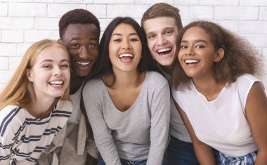 Portrait of happy multiethnic young friends students having fun over white wall background, close up