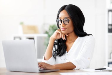 İş yerinde dizüstü bilgisayar kullanan, belge yazan, çevrimiçi iş toplantısına katılan pozitif kadın yönetici. Genç siyahi girişimci Webinar projesine katılıyor.