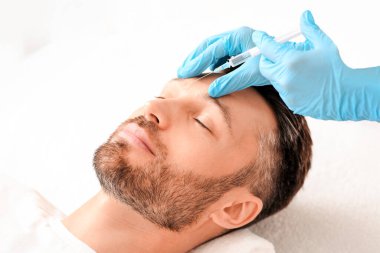 Tanımlanamayan kozmetolog koruyucu eldivenleriyle kaşlarını çatma çizgilerine karşı dolduruyor. Klinikte kaldırma işlemi gören orta yaşlı bir adam, kopyalama alanı