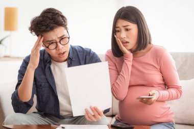 Aile Finansal Krizi. Faturaya bakan üzgün Asyalı çift evdeki koltukta oturan faturaları ödeyemiyor. Eşler Coronacrisis 'ten muzdarip, Mali Borç Sorunları Yaşıyor