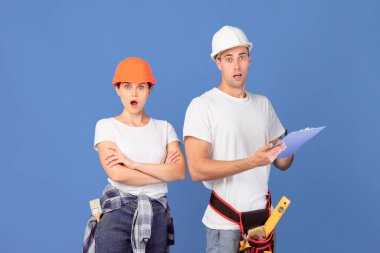 Koruyucu şapkalı Şok Adam ve Kadın 'ın portresi, yenilenme için büyük bütçeye duygusal tepki, açık ağızlı, mavi arka planda boş bir alanda duran şaşaalı çift.