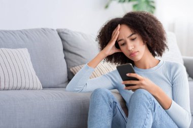 Sorunlar, kötü haberler, kendini soyutlama sırasında evde negatif duygular. Üzgün Afro-Amerikan bayan akıllı telefonuyla yazı yazıyor ve kafa kafaya verip oturma odasının iç kısmında, kanepenin yanında oturuyor.