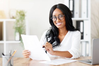 Ofisteki evraklarla çalışan güzel siyahi iş kadını. Afrika kökenli Amerikalı kadın girişimci işyerinde önemli bir sözleşme ya da anlaşma arıyor