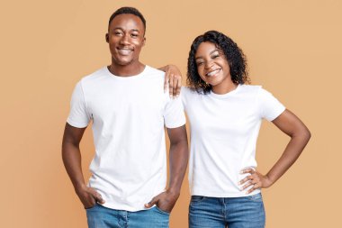 Cheerful black guy and his happy girlfriend posing on yellow studio background, copy space. Smiling african american couple bonding and posing at camera. Love, relationships, family concept