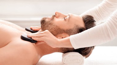 Erkekler için Tayland spa 'sı. Tanımlanamayan kadın terapist rahat erkek omuzlarına siyah taşlar yerleştiriyor. Orta yaşlı zengin bir adam sıcak taş masajı yaptırarak erkek kaplıcasında gününü gün ediyor.