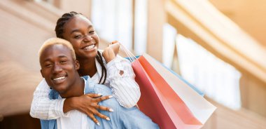 Boş zaman, boş zaman ve satın alma. Gülümseyen Afro-Amerikan çifti kağıt torbalarla mağazanın yanında eğleniyorlar, güneş parlıyor.